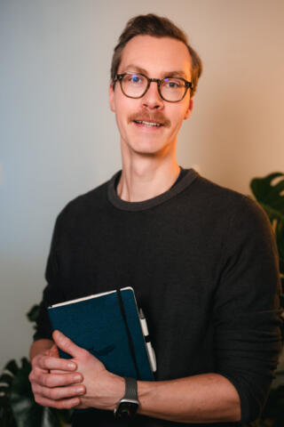 Frank Wesneck mit einem blauen Notizbuch und freundlicher Blick in die Kamera.